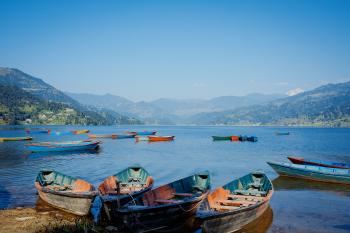 A colour photo of several colorful boats at the edge of a lake among the mountains. Pokhara, Nepal, 2009.