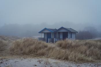 A colour photo of two beach huts in the fog, brown grass in front